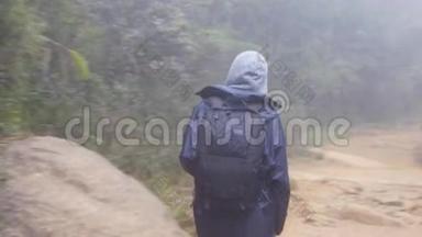 带着背包的旅游女孩在热带森林漫步。 穿着雨衣在潮湿的树林里散步的女人
